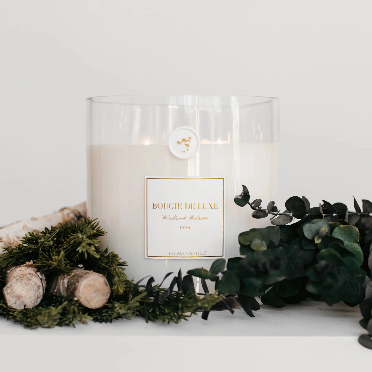 large white candle displayed with eucalyptus and greens