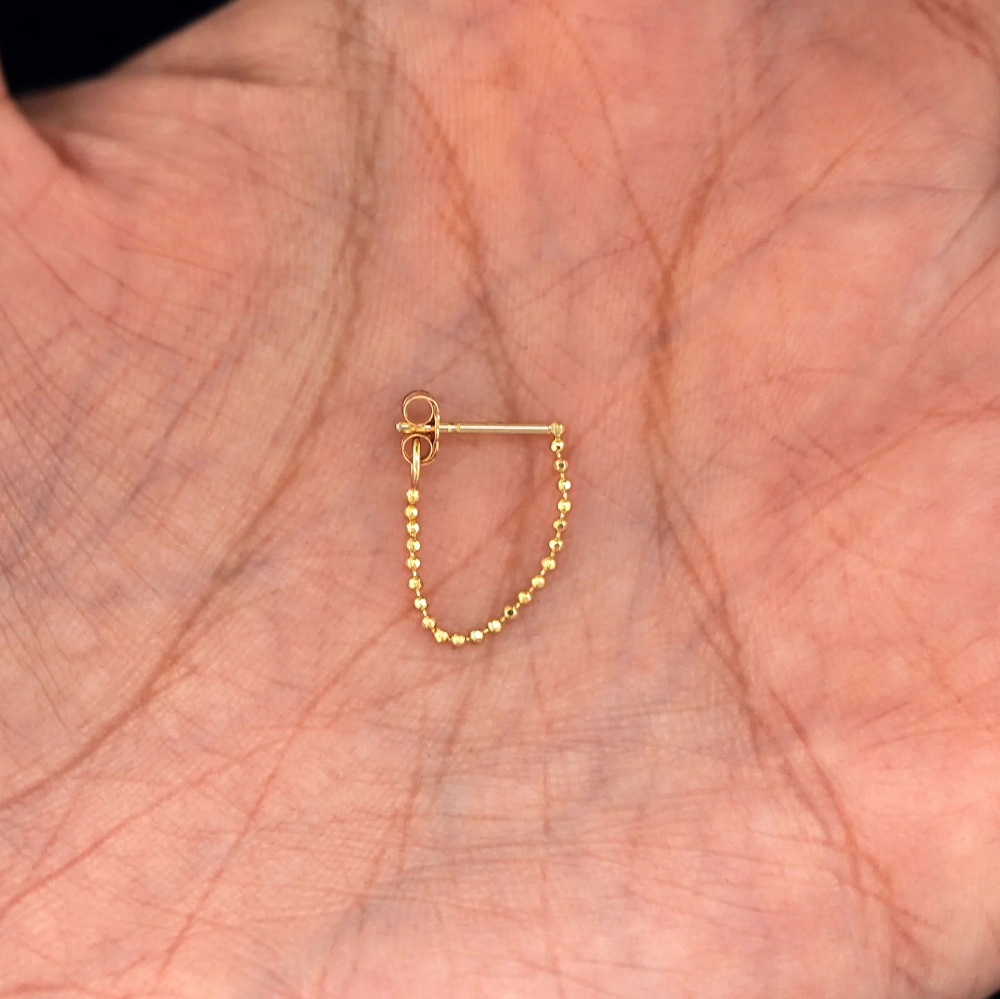 stud and chain earring on display in a hand
