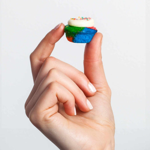 person holding a mini tye dye cupcake between their thumb and pointer finger