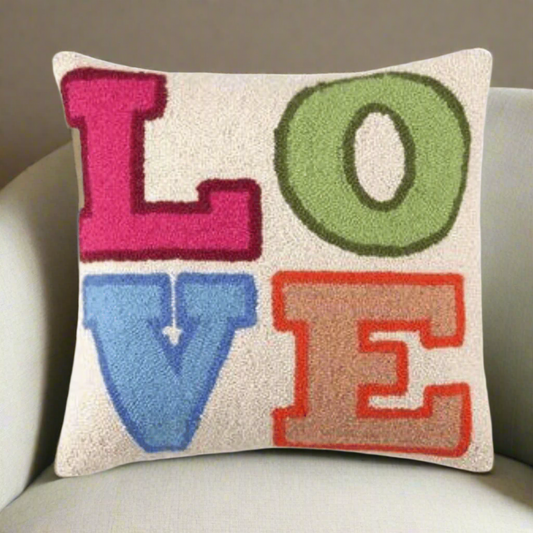 close-up of LOVE pillow in pink orange blue and orange colors aginst chair