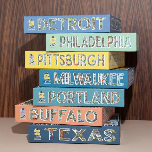 boxes of city puzzles stacked on top of each other--Texas, Buffalo, Portland, Milwaukee, Pittsburgh, Philadelphia, Detroit