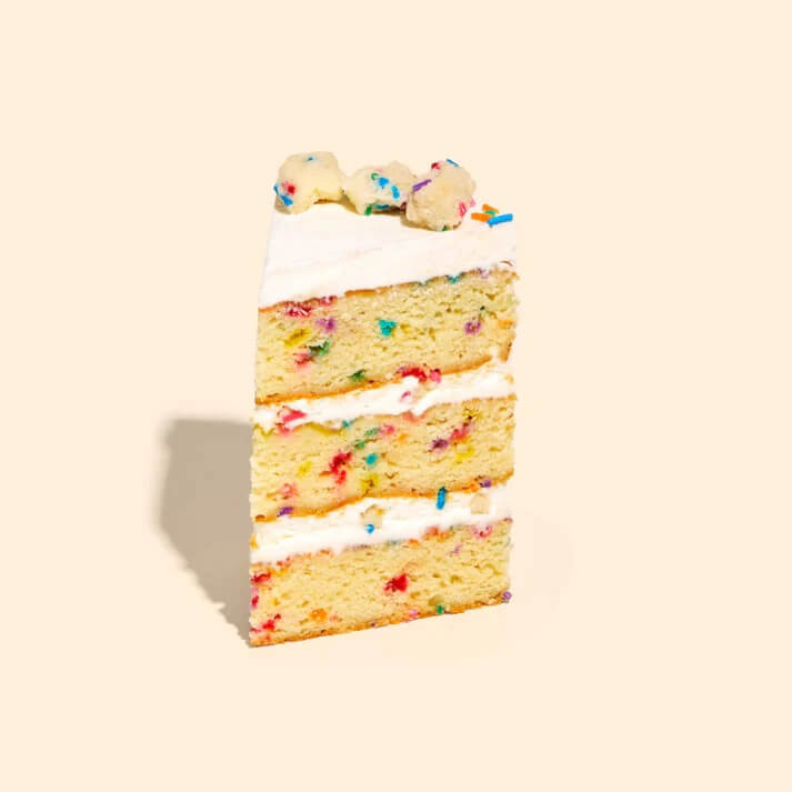 slice of milk bar birthday cake with layers of cake and frosting with cake balls and sprinkles on top