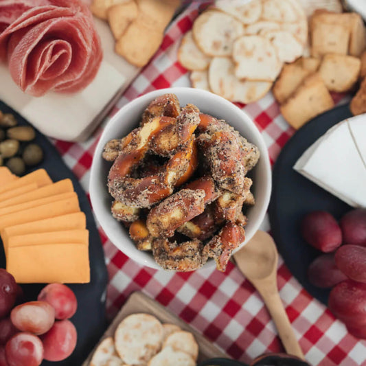 Pretzels in a bowl with charcuterie items on a red and white checkered tablecloth